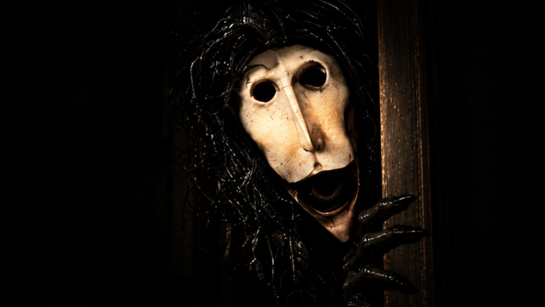 The creature's masked face and long-fingered hand gripping the edge of a door as it opens.